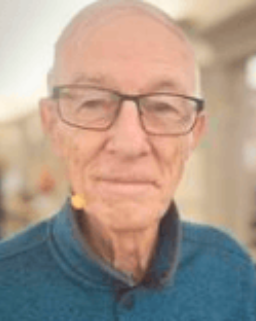 Older man wearing glasses and a blue sweater, looking at the camera indoors.