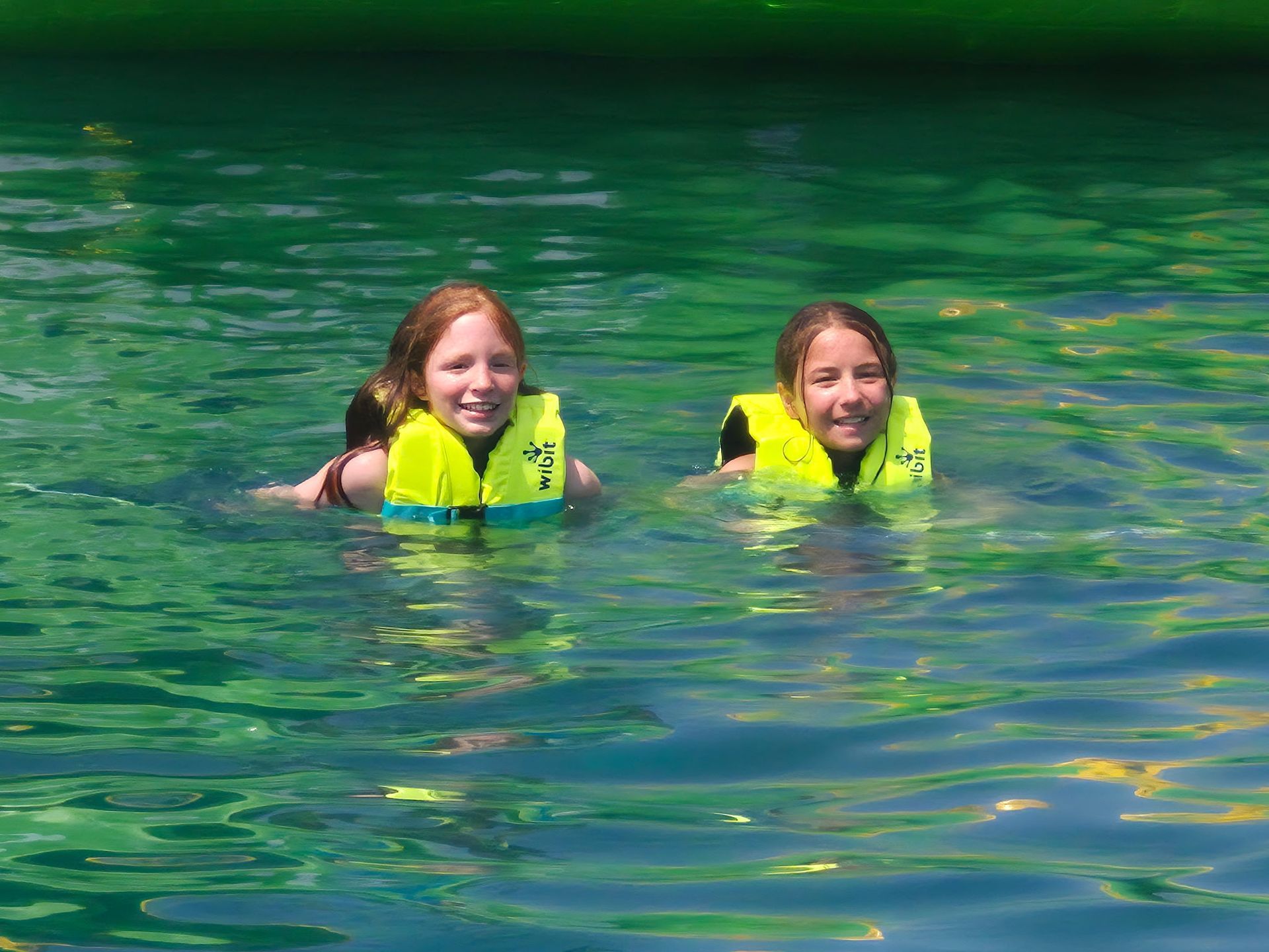 Two people in yellow life vests smiling while floating in green water