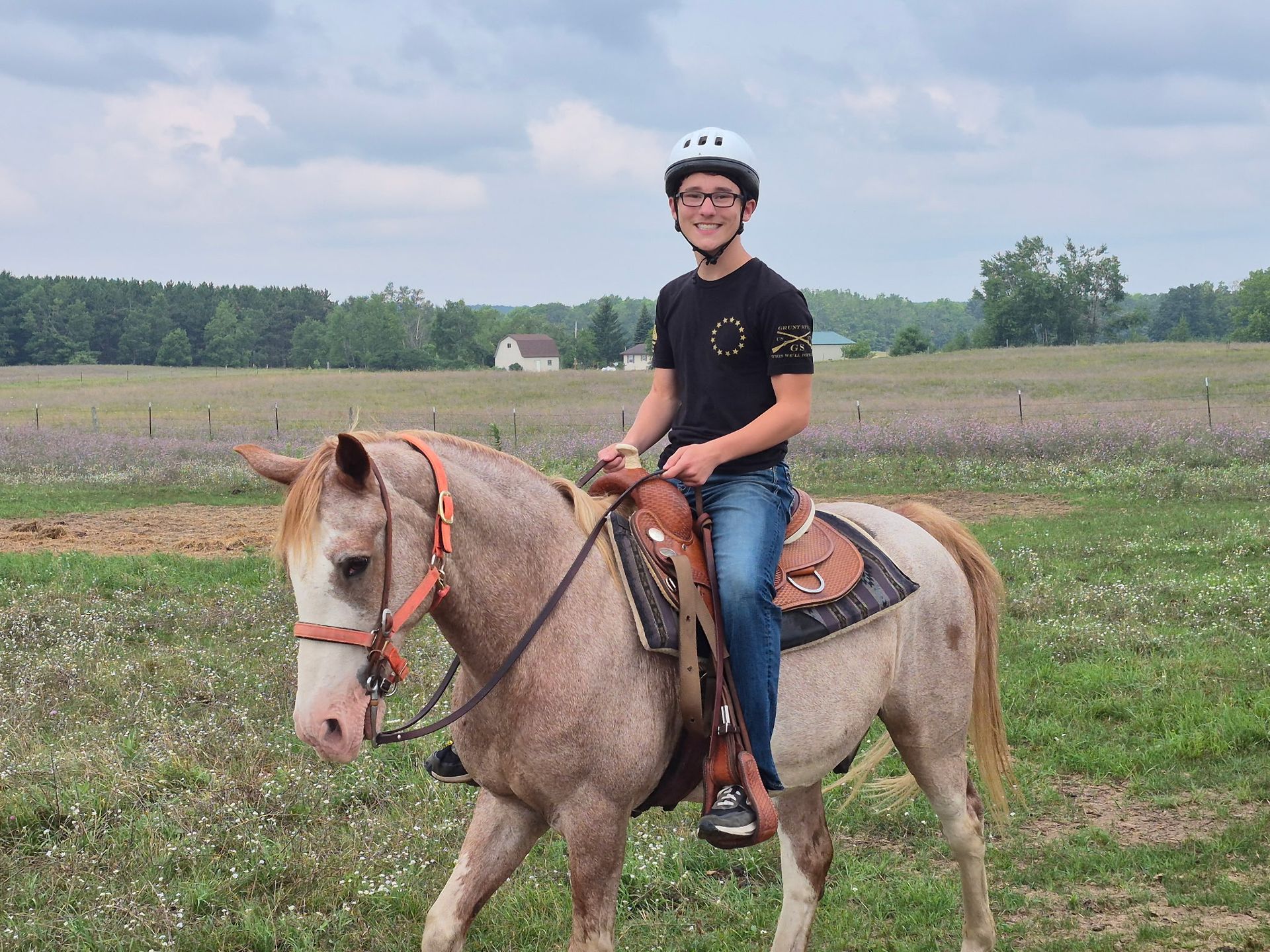 Person riding a light horse in a field, wearing a helmet and smiling.