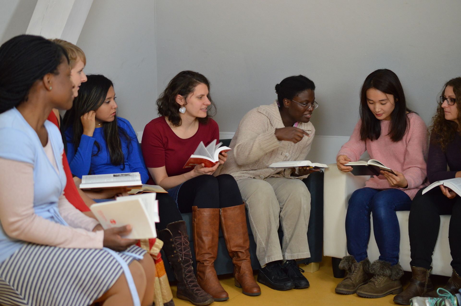 Five people sitting in a circle, reading and discussing books in a small meeting room.