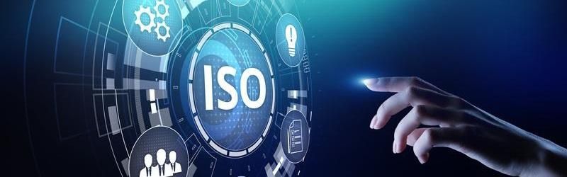 Hand pointing towards a glowing blue ISO symbol with technical icons in the background on a dark blue gradient.
