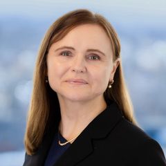 A portrait of Anna Mumford, Cybersecurity at CONNSTEP, in a black blazer smiling, looking at the viewer. Background: blurred cityscape.