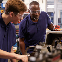Two people wearing safety glasses working with machinery in a workshop.