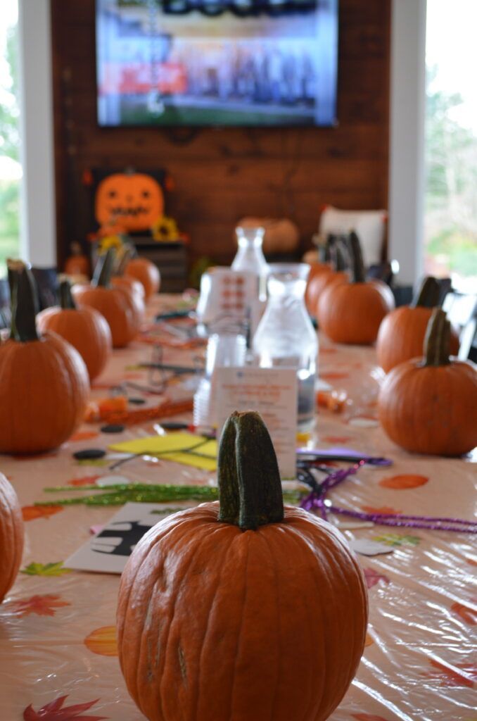 Pumpkins line a table decorated for Halloween, with milk bottles and decorations in the background.