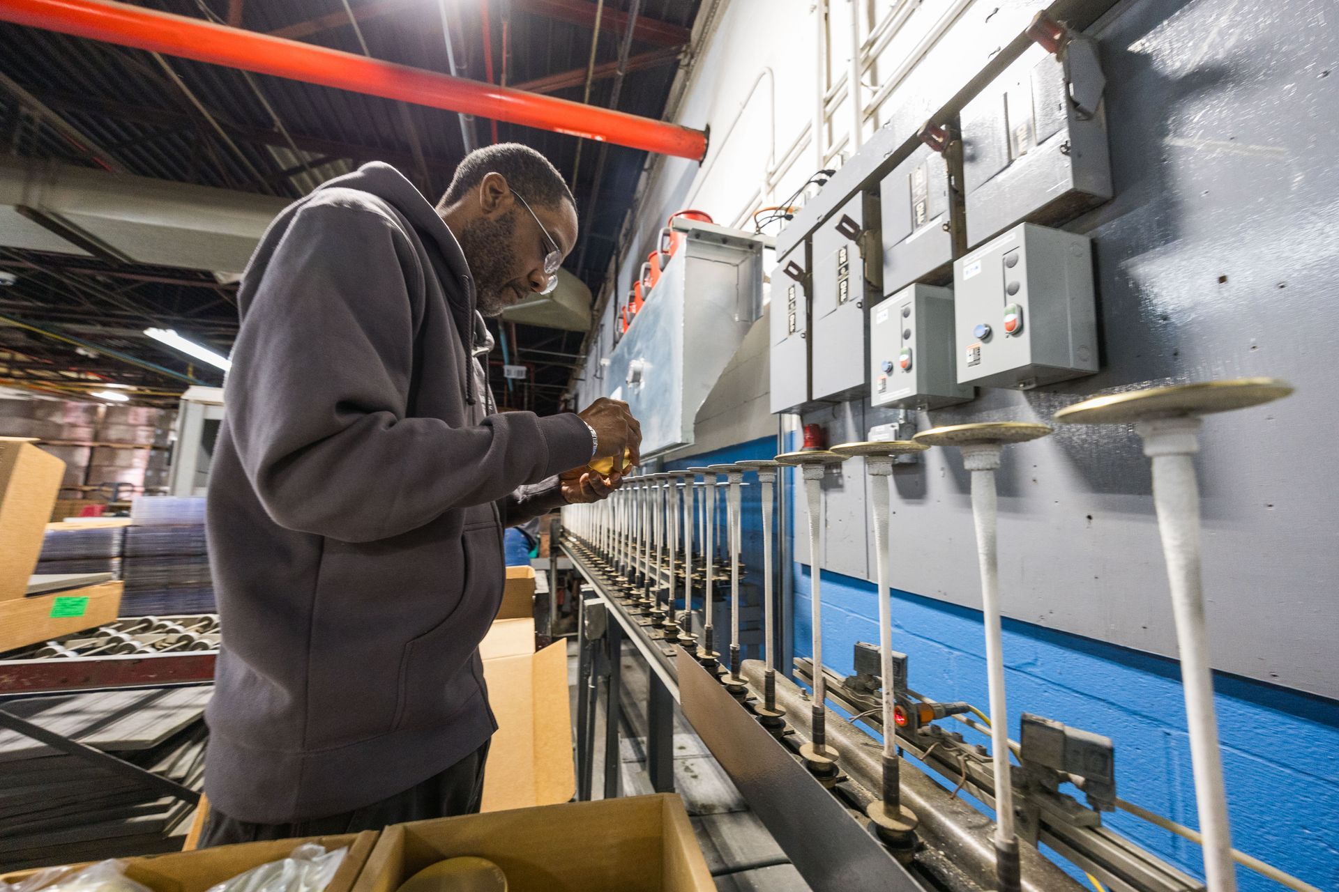 Worker in grey sweatshirt inspects objects on a production line in a factory.