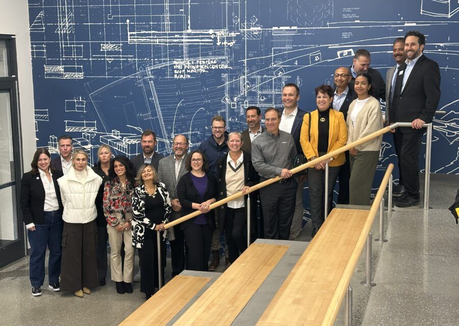 Group of people posing on stairs in front of a blueprint-covered wall.
