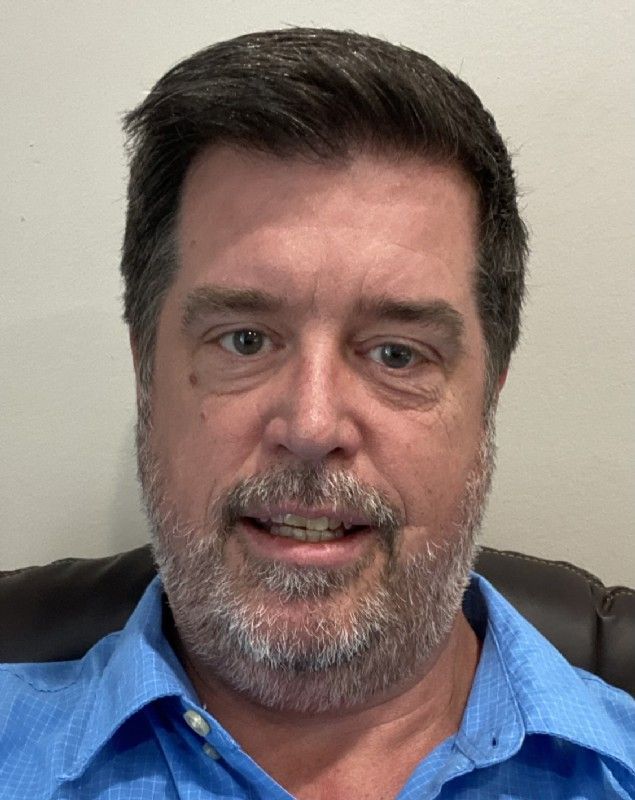 A man with a beard and a blue shirt is smiling for the camera.