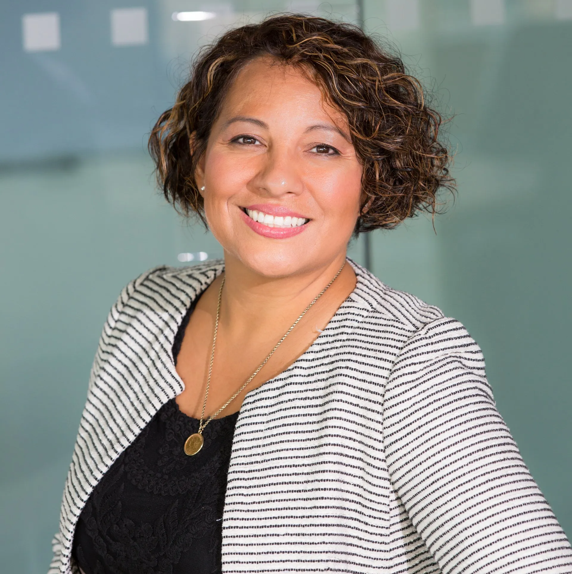 A woman wearing a striped jacket and a black shirt is smiling for the camera.