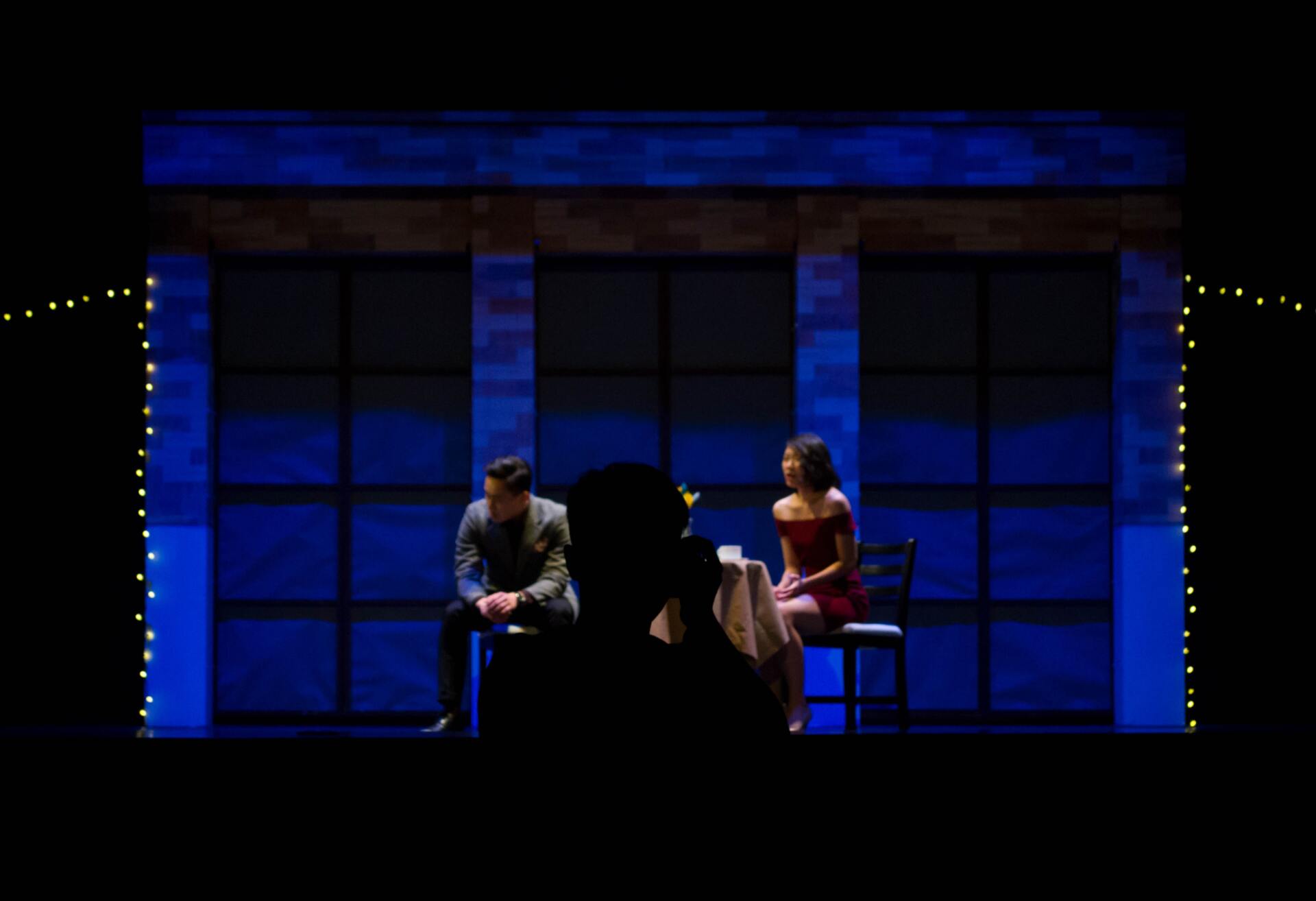A man and a woman are sitting on a stage with blue lights behind them.