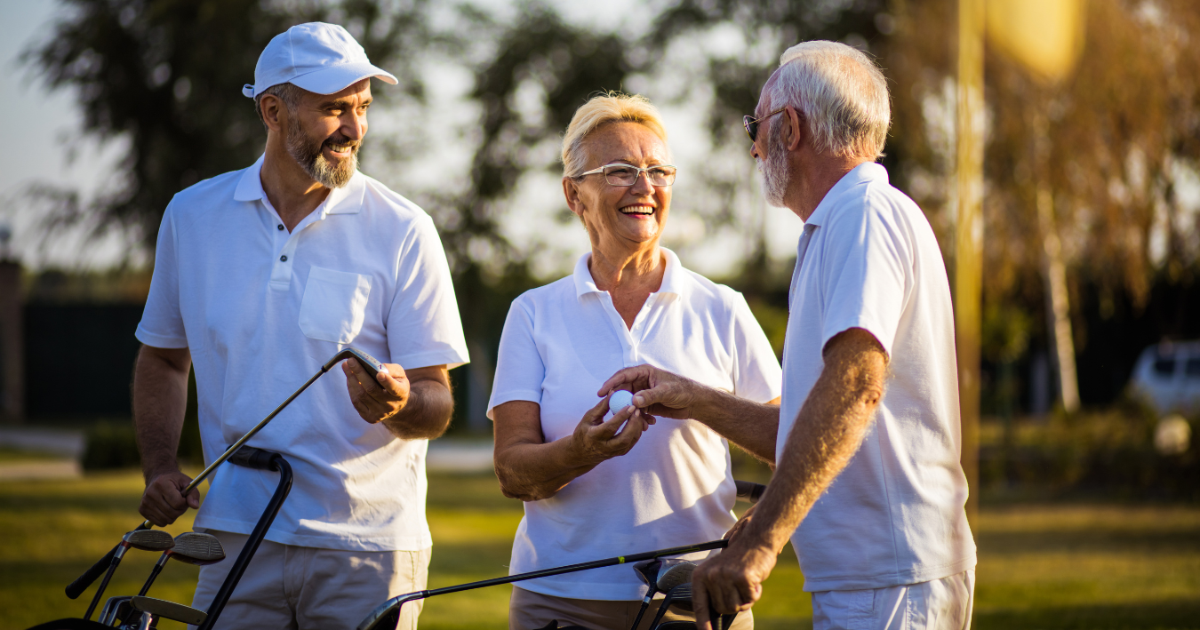 Three people talking on golf course at sunset, holding clubs and smiling