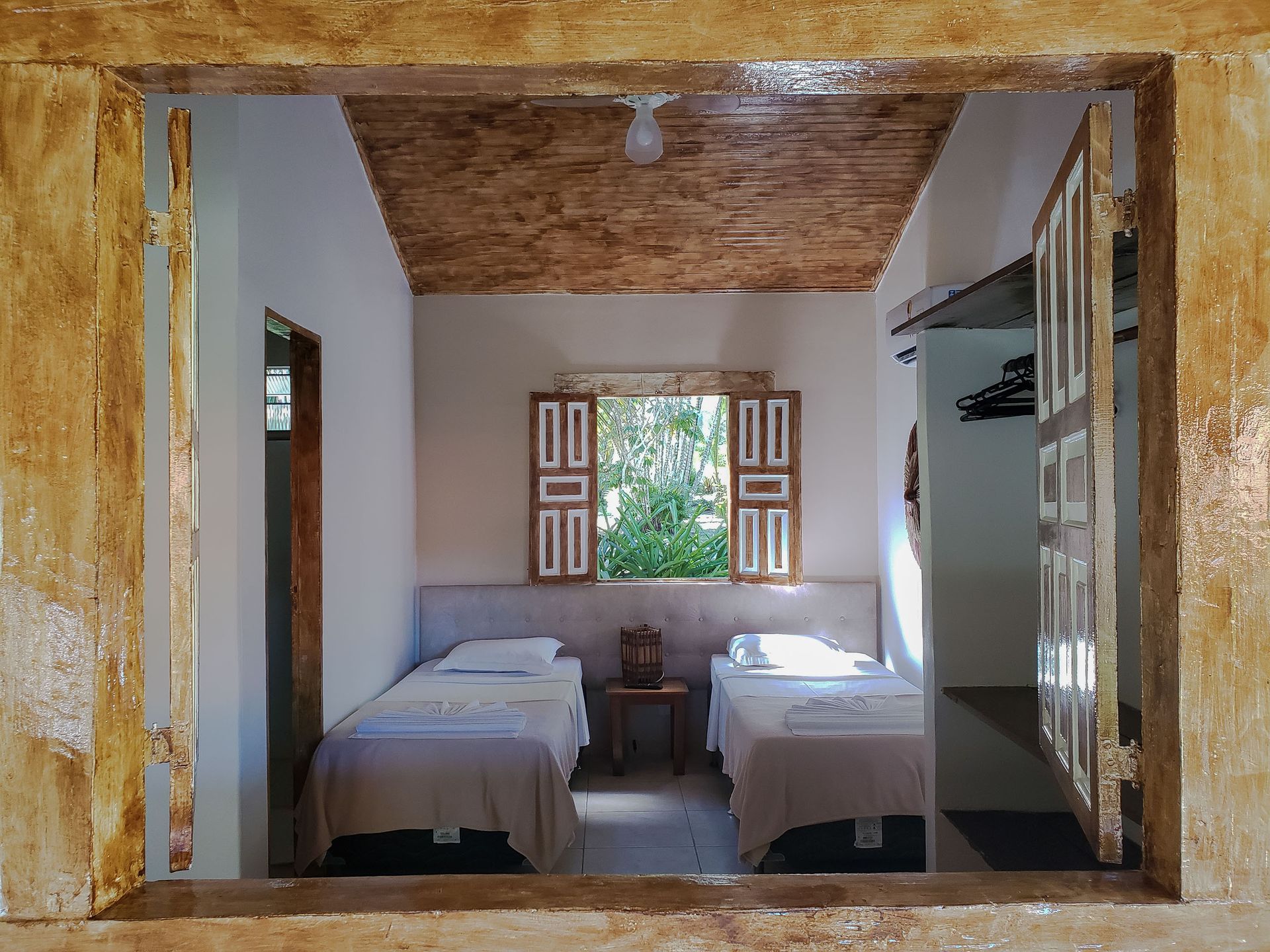 Quarto pequeno com duas camas de solteiro, uma janela e um closet aberto.