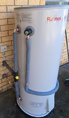 Rinnai water heater. Silver tank with insulated pipes, against a brick wall.
