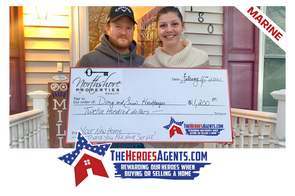 A man and a woman holding a cheque in front of a house