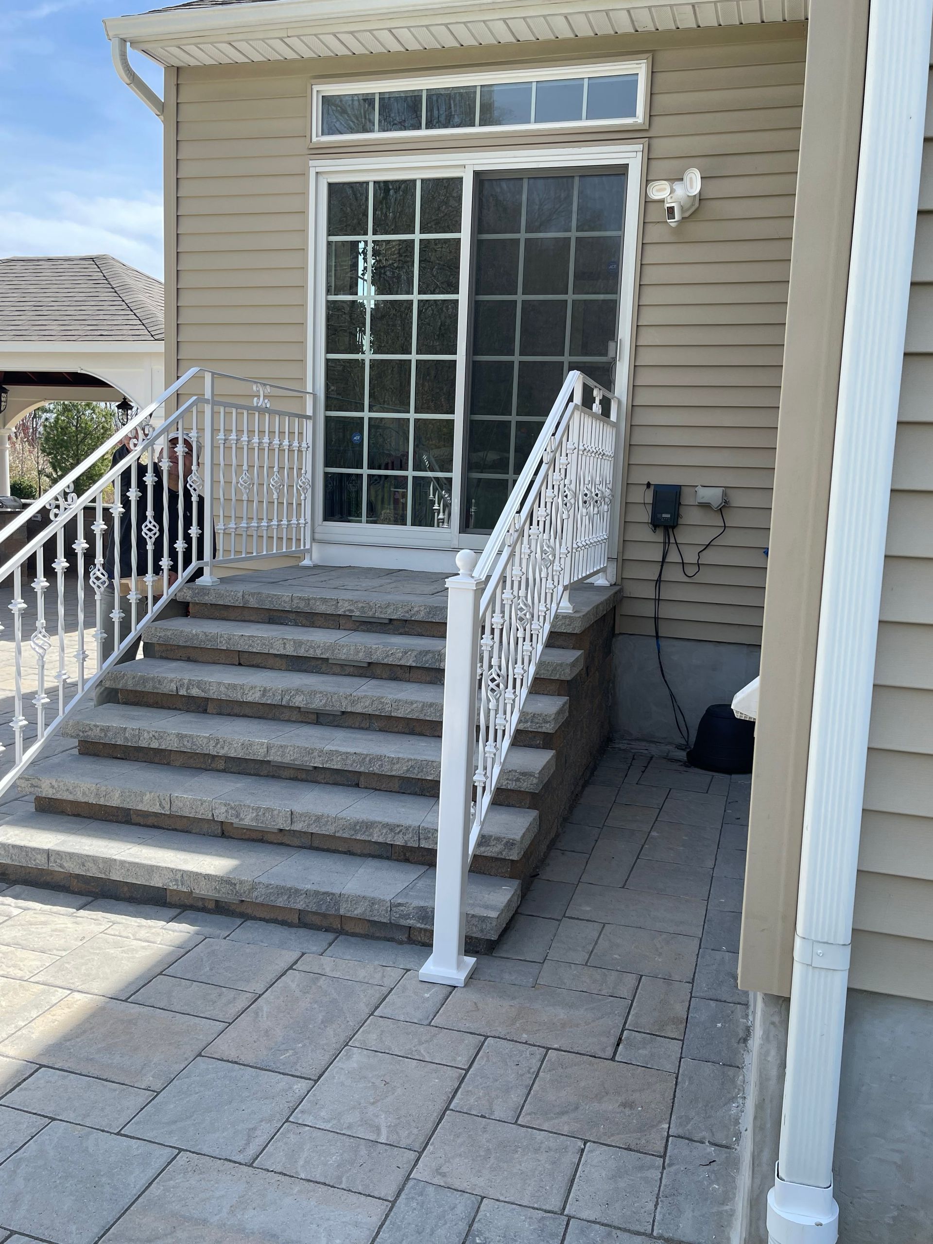 Front entrance with gray steps, white railings, and sliding glass doors on a tan house