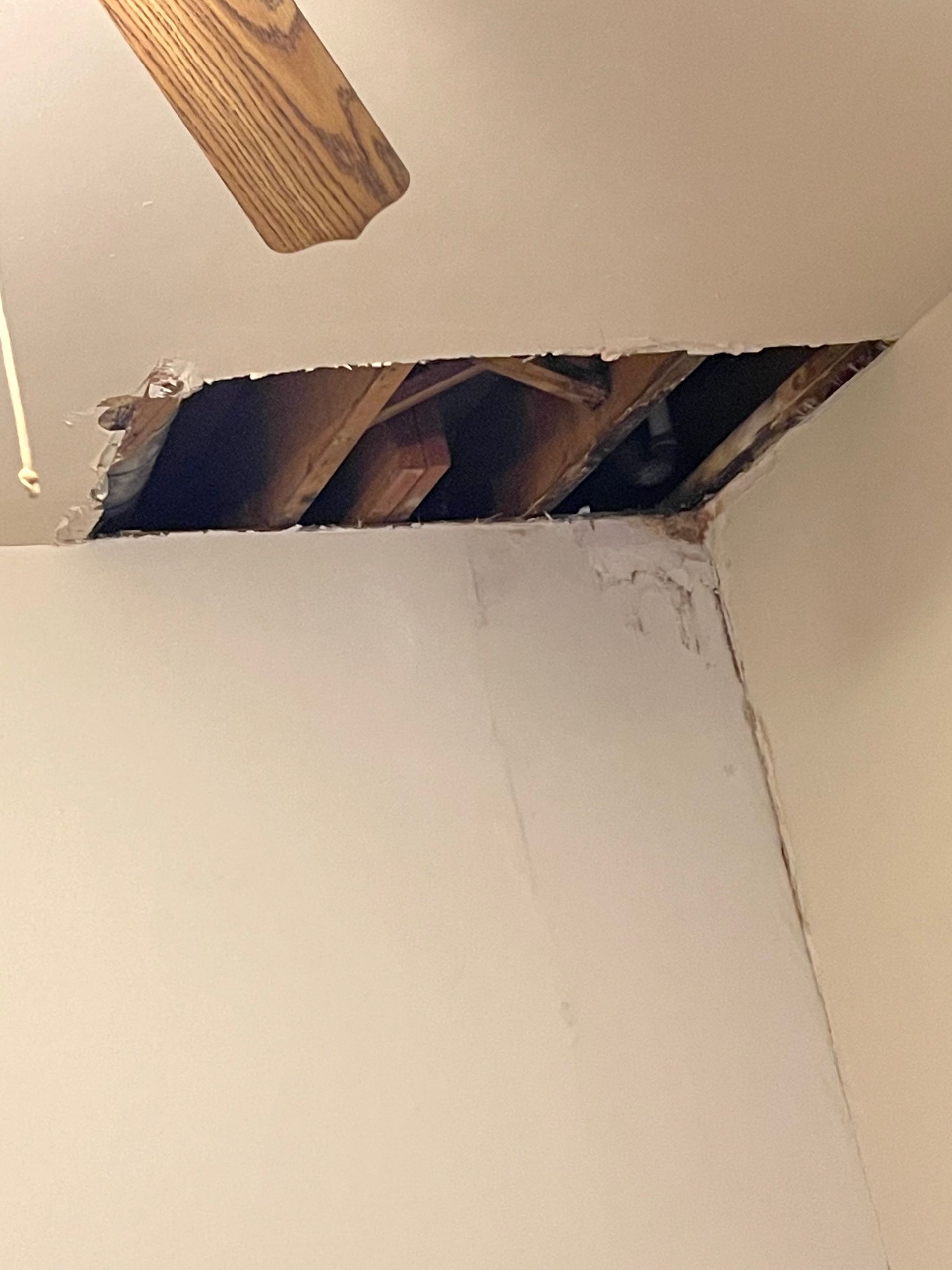 Ceiling hole exposing wooden beams above a white wall with peeling paint