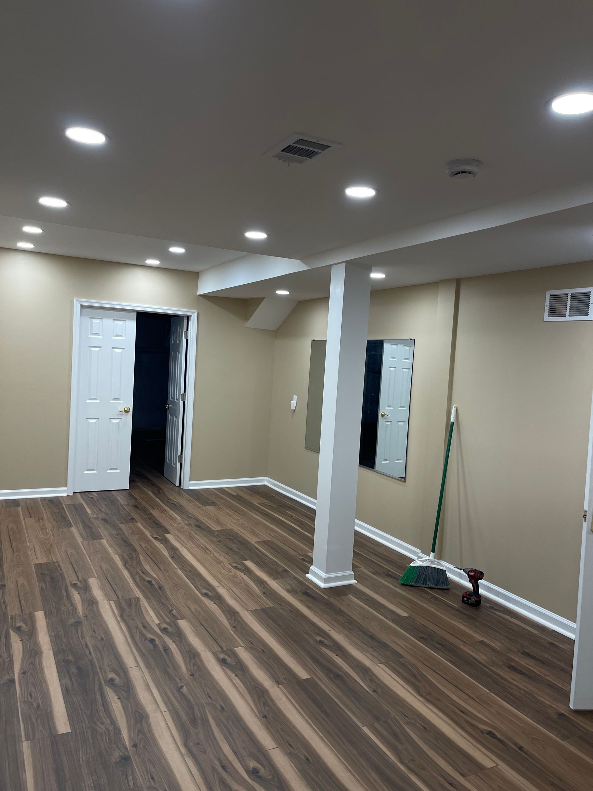 Empty renovated room with wood-look flooring, recessed lights, white columns, and a broom near the wall