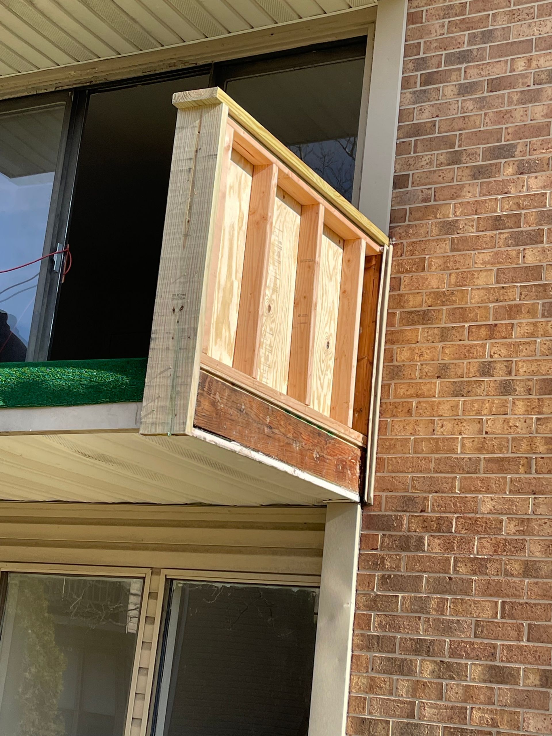 Close-up of a brick apartment balcony with a wooden privacy panel and screened window.