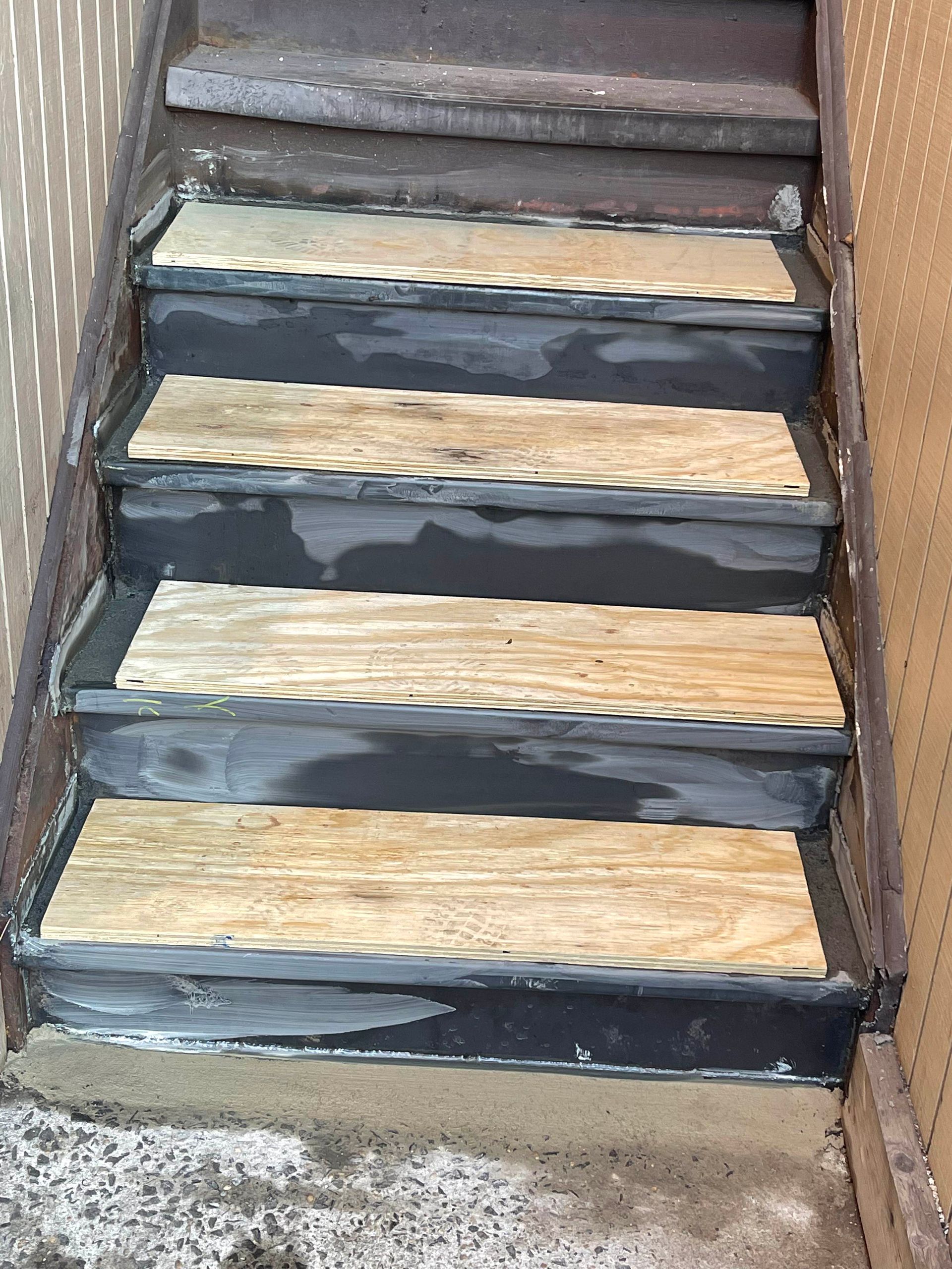 Weathered wooden staircase with peeling dark paint and worn steps between brick walls