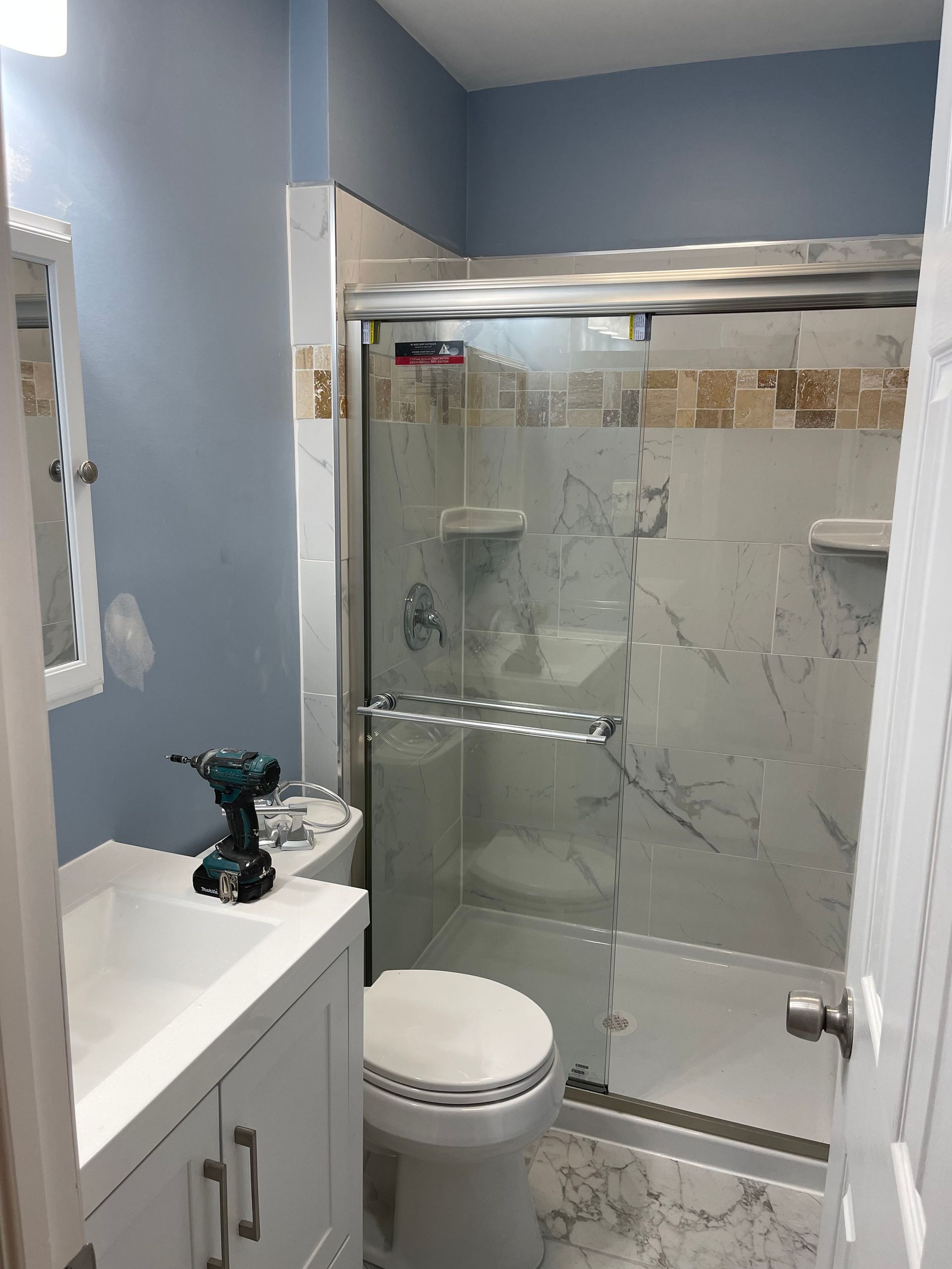 Small bathroom with blue walls, white vanity, toilet, and a glass-enclosed shower.