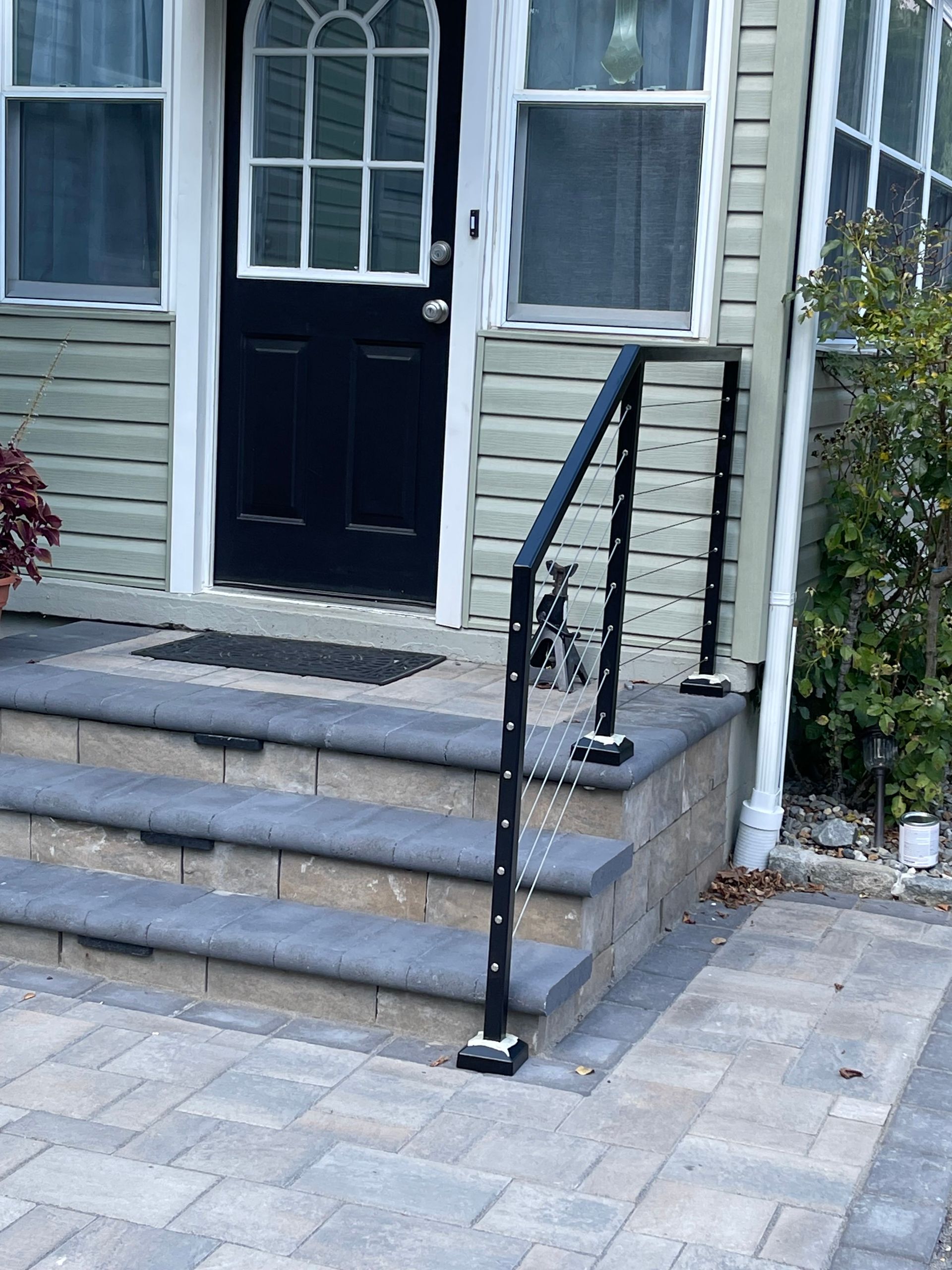 Front steps with black handrail leading to a house’s front door and windows