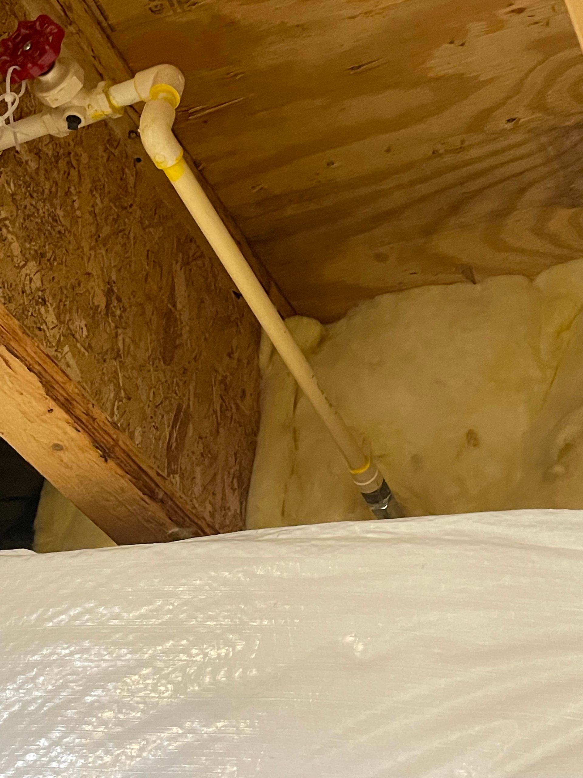 Insulated attic with a white PVC pipe running into foam insulation near a wooden beam.