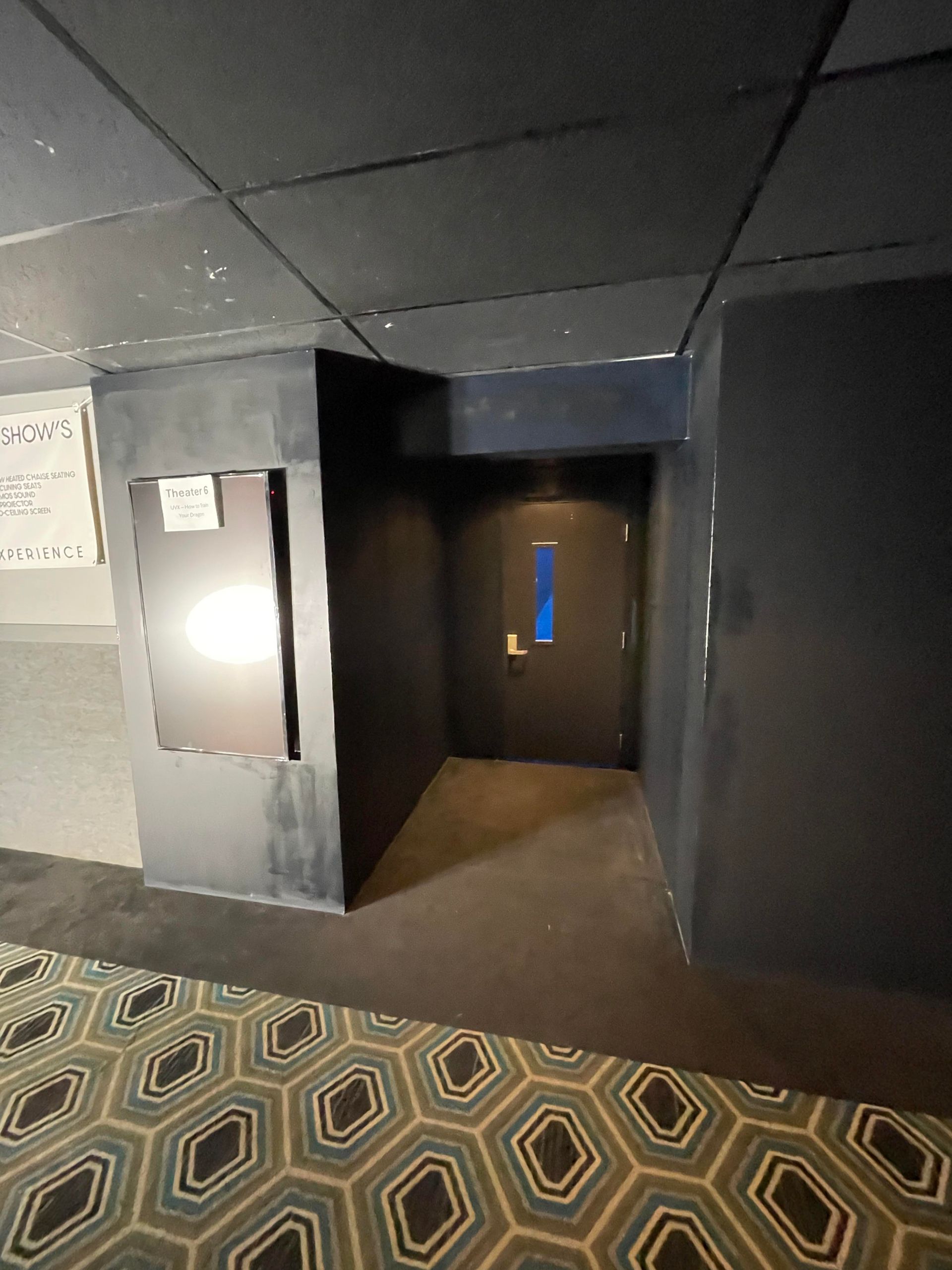 Dark theater entrance with a lit doorway and patterned carpet in the foreground