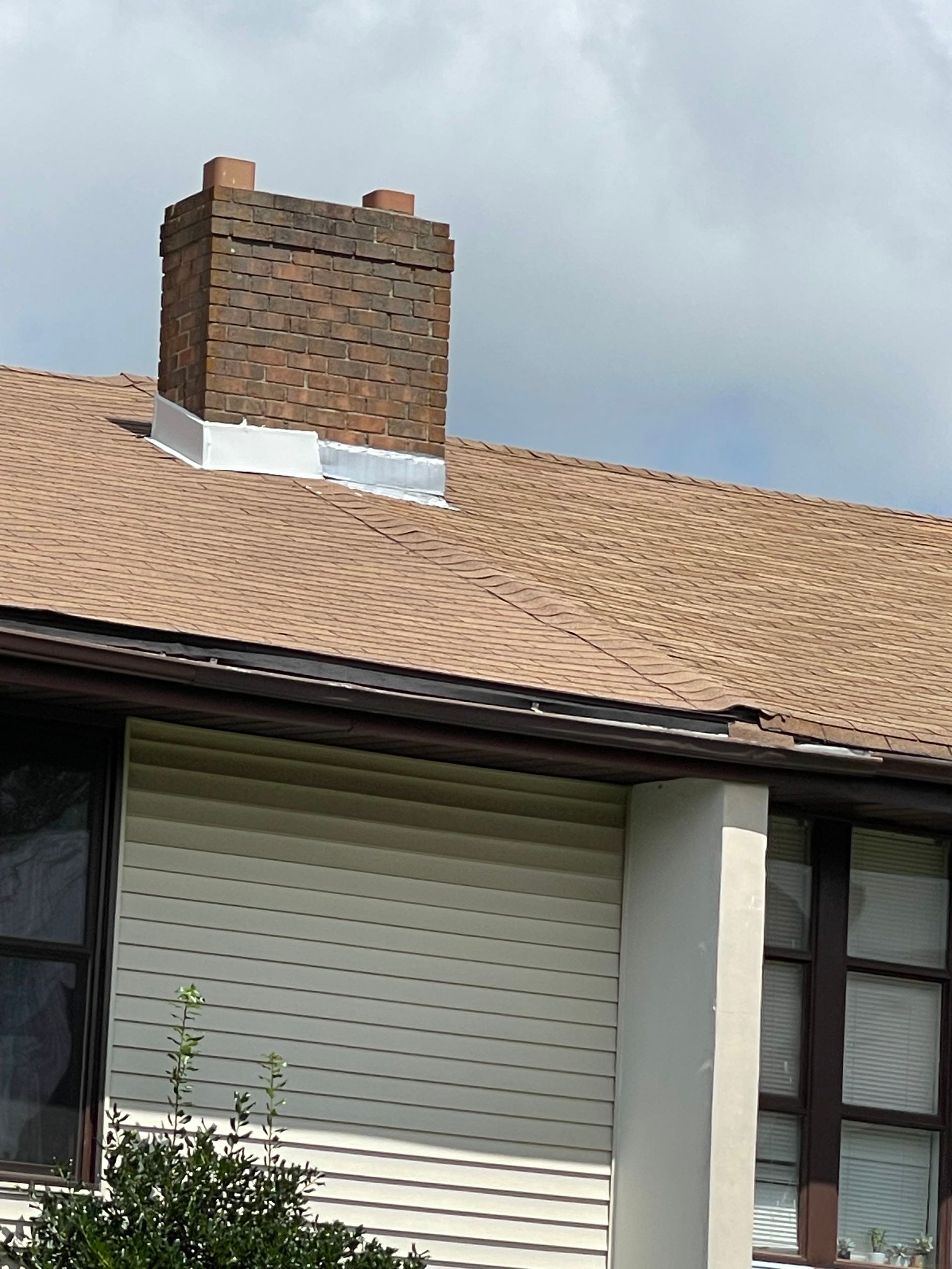 Brick chimney above a tan tiled roof and white house siding under cloudy sky