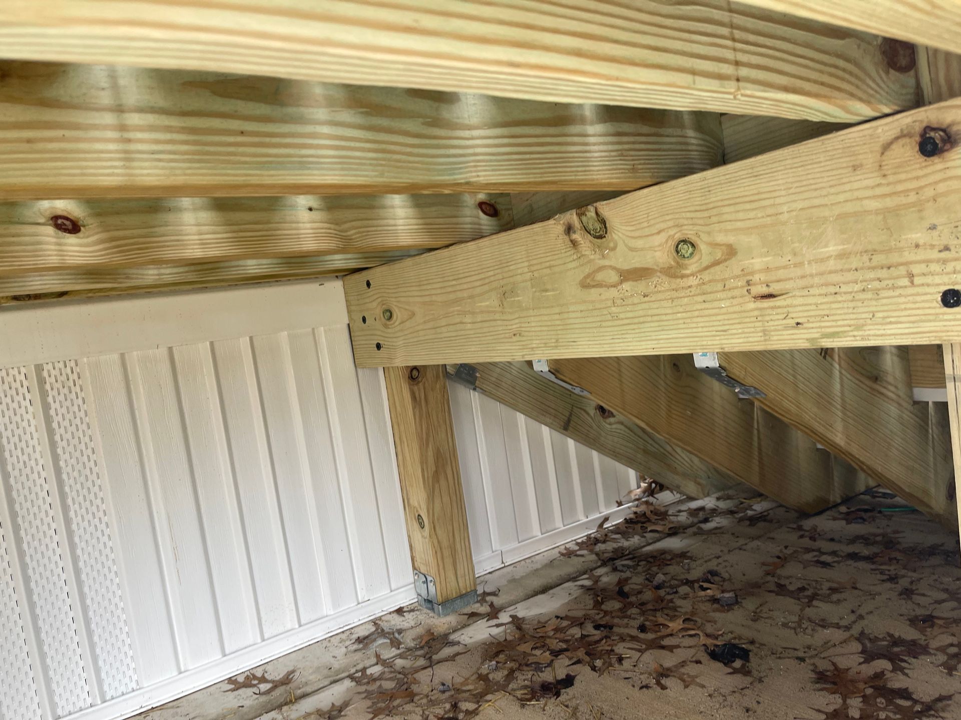 Under-bed wooden support beams over a leaf-covered floor in a small crawlspace
