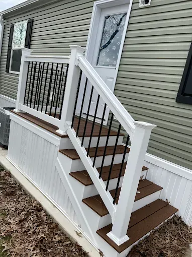 Front porch stairs with white railing, brown steps, and a white door on a beige house.