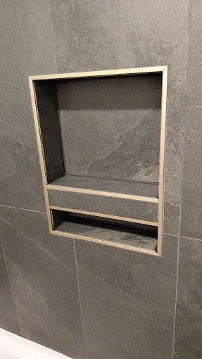 Recessed wall niche with gray tile, featuring a shelf and a narrow lower opening