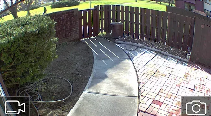 Curved concrete walkway beside a brick patio and wooden fence in a sunny backyard