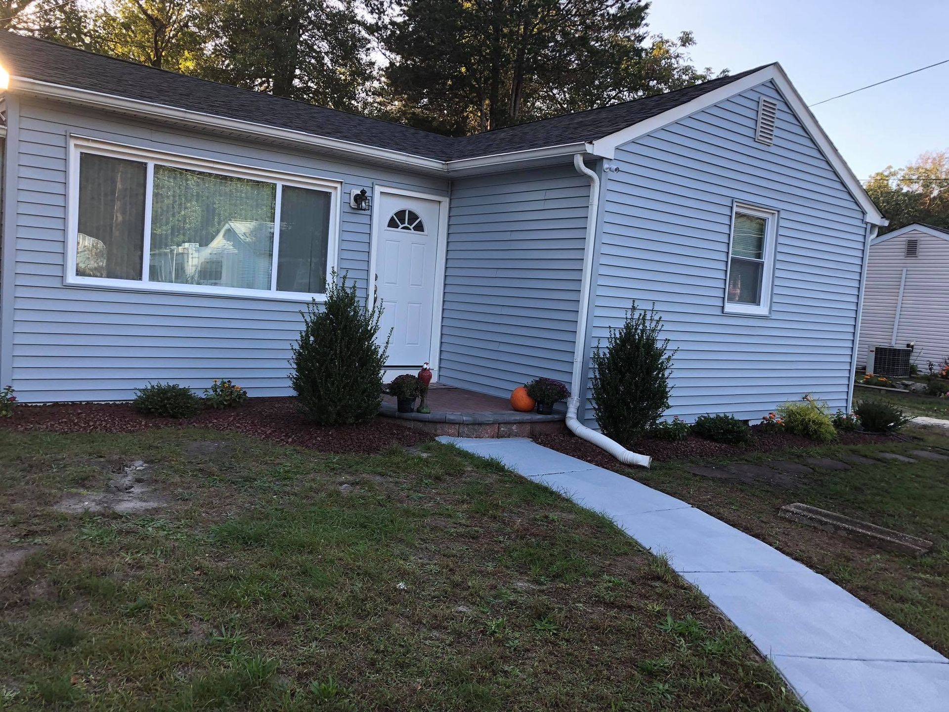Single-story blue house with white trim, front lawn, and a curved concrete walkway leading to the door