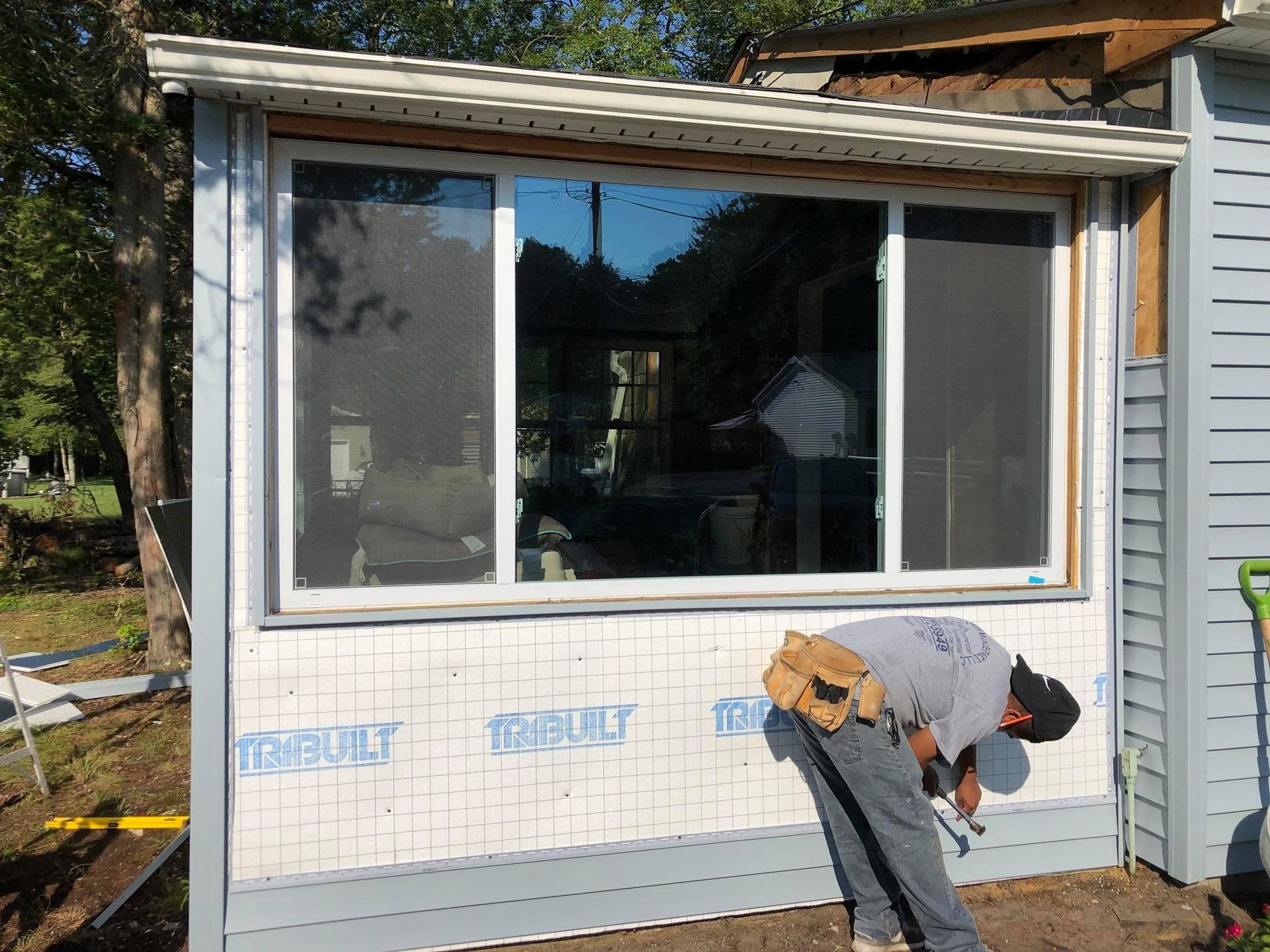 Worker installing exterior siding below a large window on a house addition.