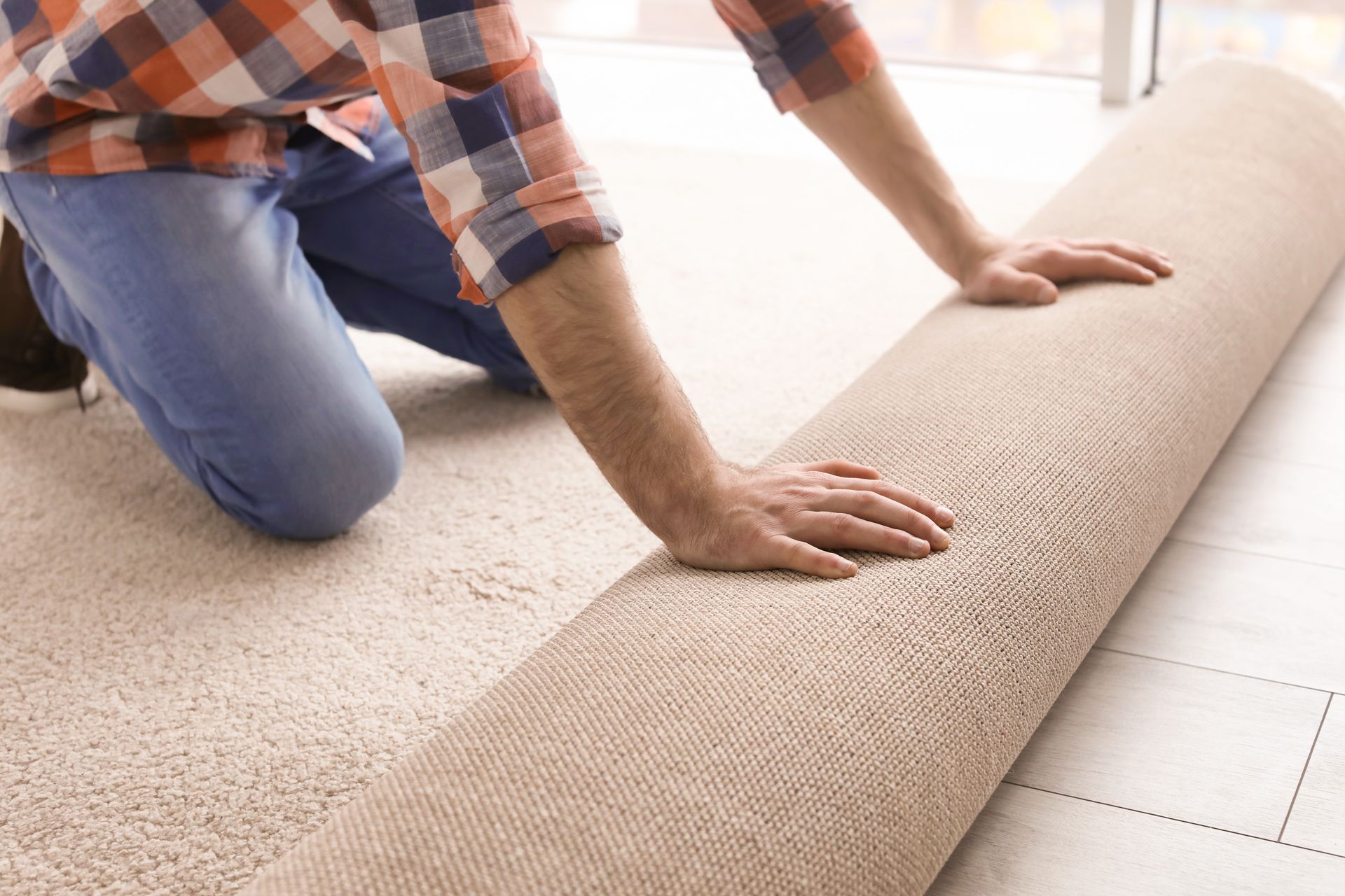 Person rolling out beige carpet in a bright room