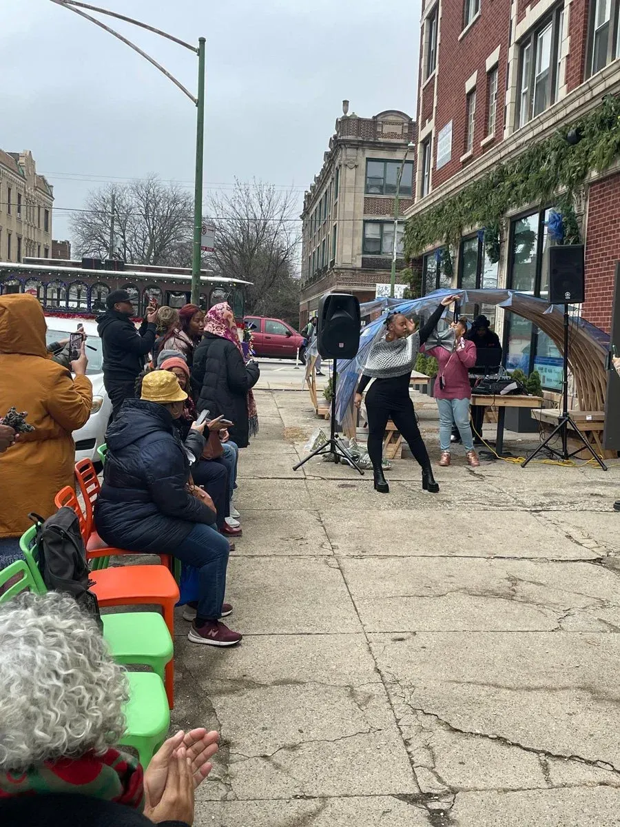 Outdoor market stall with people seated and standing on a city sidewalk beside brick buildings