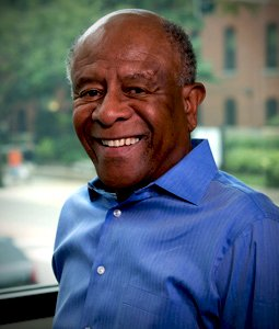Man in a blue shirt smiling. Sunlight is in the background.