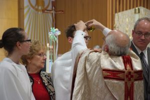 Priest in white and red vestments raises a host during a church service beside two congregants