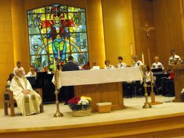 Church altar with several clergy seated before a colorful stained-glass window during a service