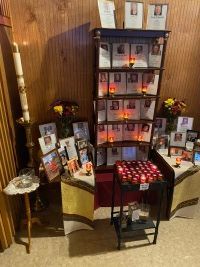Memorial altar with framed photos, candles, flowers, and red votives against a wood-paneled wall