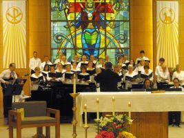 Choir singing in a church sanctuary with a stained-glass window behind the altar