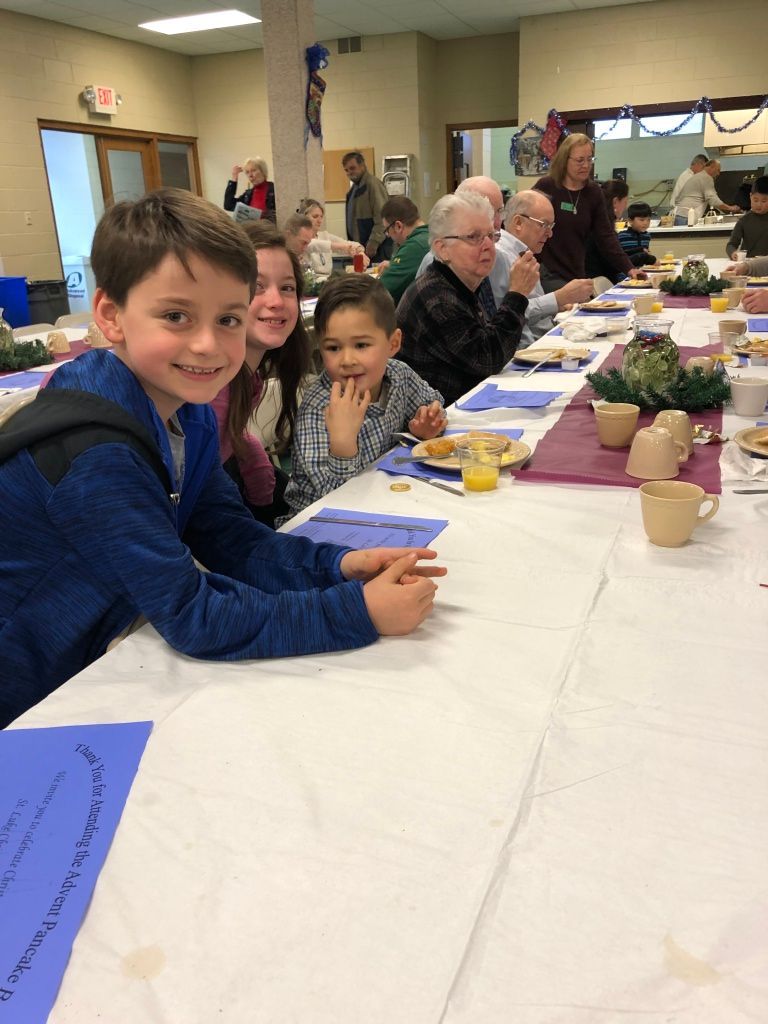 Children seated at a long table during a community meal, smiling toward the camera.