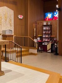 Church interior with wooden pews, a lectern, and a lit display screen near a pamphlet stand.