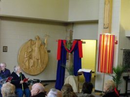 Church stage with blue drapes, red cloth, wall relief, and people seated in front