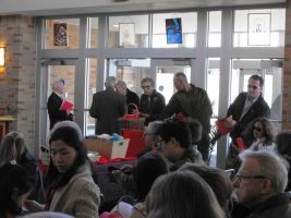 People gathered in a bright indoor room around tables and red gift bags, chatting near large windows.