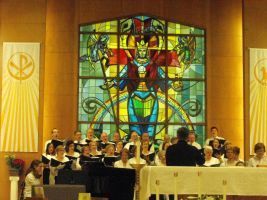 Choir performing in a church before a large colorful stained-glass window of Jesus