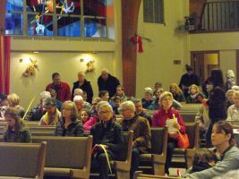People seated in a church sanctuary, with stained glass windows and wooden pews.