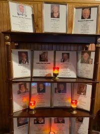 Memorial display with framed photos and lit candles on shelves in a wooden corner cabinet