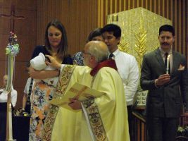Priest holding a baby during a church ceremony, with people standing behind him