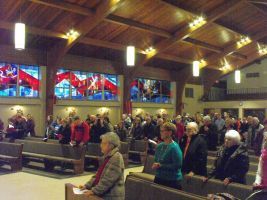 Congregation standing in a church with stained-glass windows and wooden ceiling