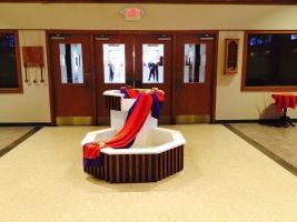 Lobby with a red, white, and blue draped display on a round pedestal near glass double doors.